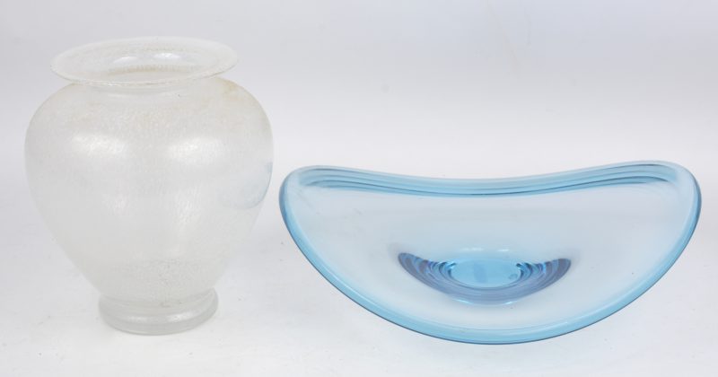 Een designschaal van blauw kristal en een vaas van kleurloos kristal met wit spikkeldecor.