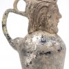 Een antiek glazen kruikje, versierd met een bebaard mannenhoofd van terracotta.