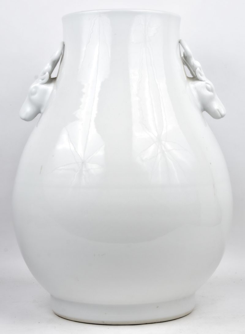 Een grote vaas van monochroom wit porselein in de geest van het blanc de Chine met handvatten in de vorm van hertenkoppen.