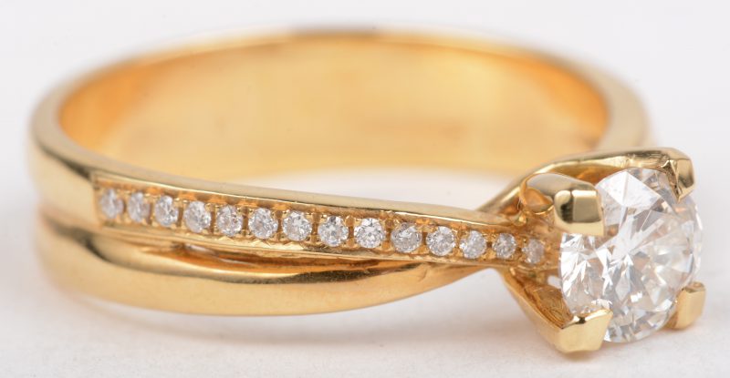 Een 18 K geelgouden ring bezet met en centrale briljant van +- 0,61 ct. en briljanten met een gezamenlijk gewicht van +- 0,14 ct.