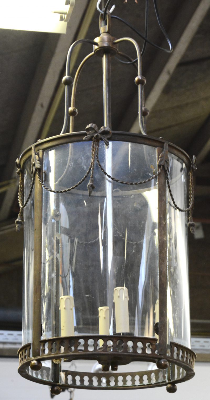 Een bronzen lantaarn met bol glas en versierd met strikken en kwispels.