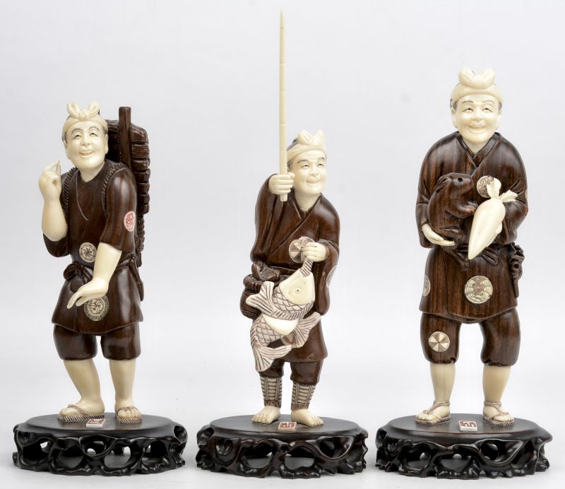Drie ambachtslieden van gebeeldhouwd en gegraveerd ivoor en kerselaar. Chinees werk naar Japans voorbeeld. Gemerkt.