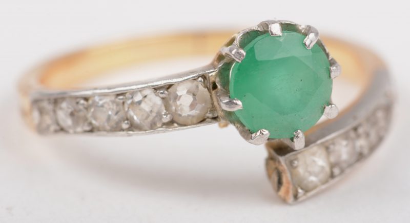 Een 18 K wit en geelgouden ring bezet met diamanten met een gezamenlijk gewicht van +-  0,30 ct. en een smaragd van +- 50 ct.