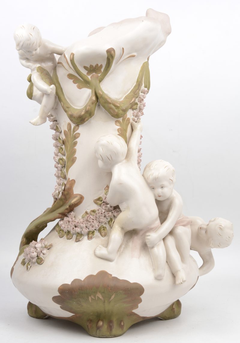 Een art nouveau siervaas van zachte pasta, versierd met kindjes en bloesems in reliëf. Bohemen, zonder merk.