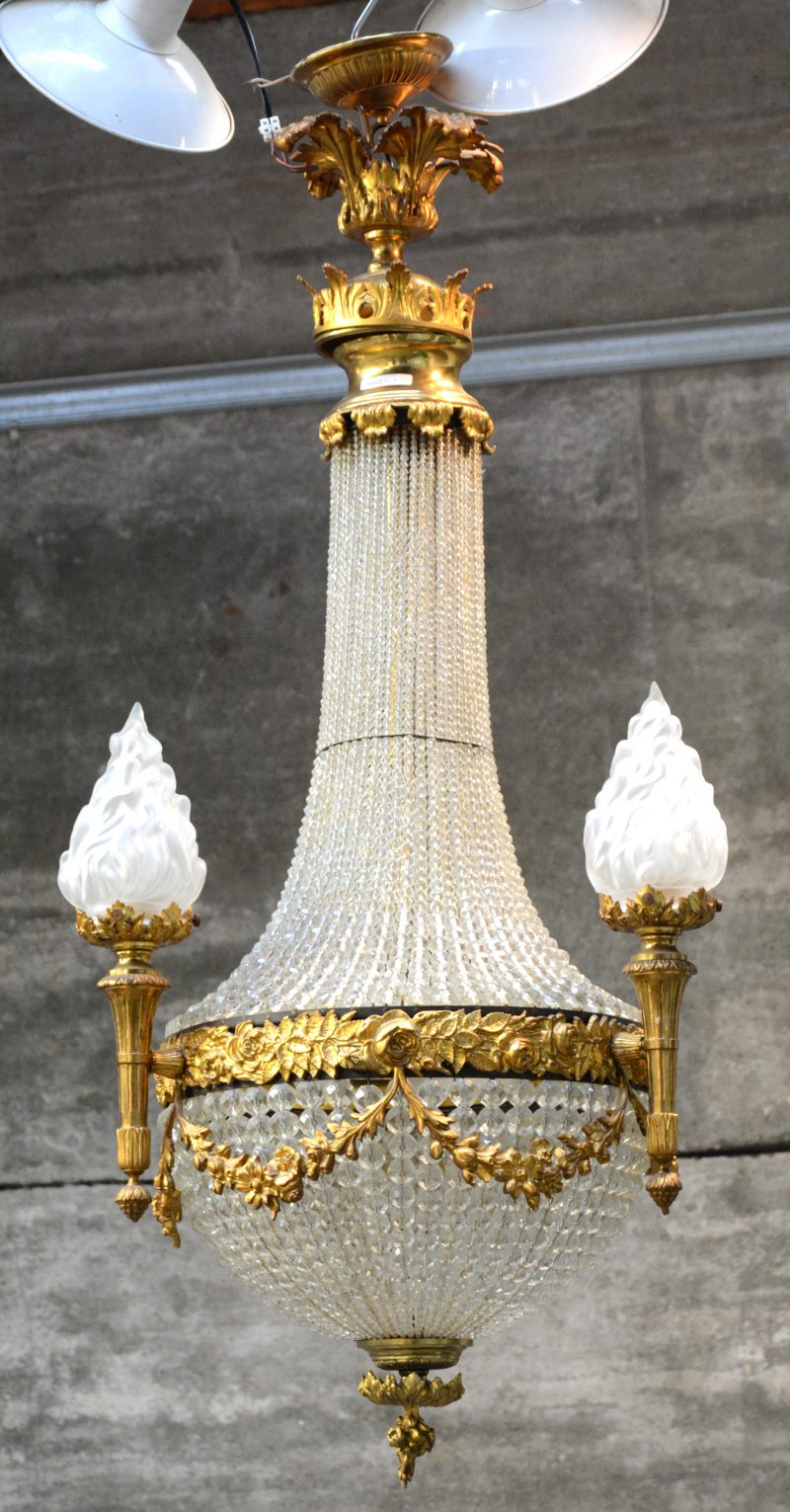 Een verguld messingen sac-à-perlesluchter met drie lichtpunten met vlamvormige gesatineerde glazen kapjes en versierd rondom met bloemenguirlandes.