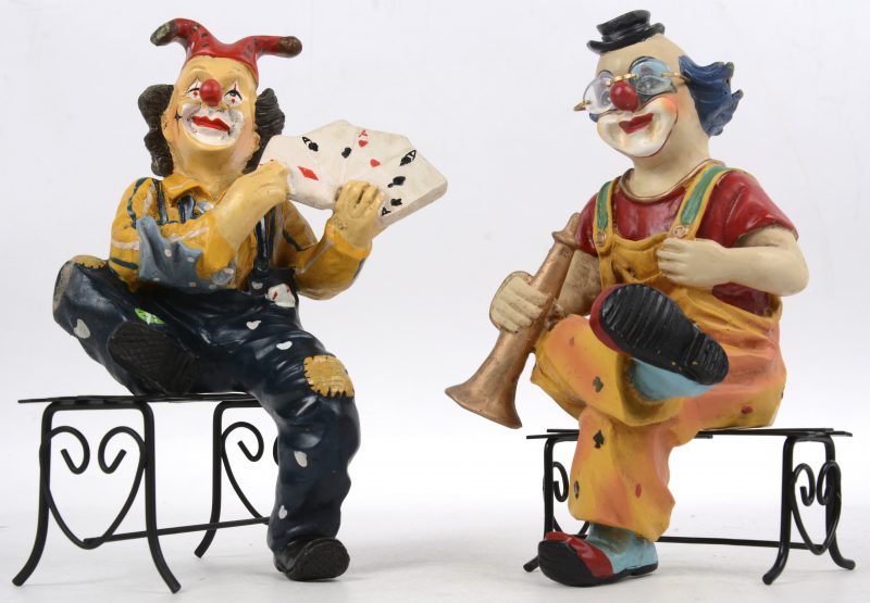 “De kaarttruck” & “De trompetist”. Twee clowns van meerkleurig kunststof op een bankje.