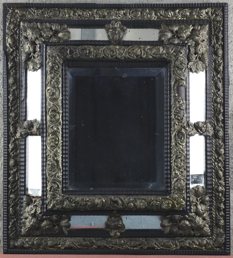 Een zwarthelakte houten spiegel, versierd met gedreven messingen beslag in de vorm van bloemen. Tijdperk barok, lichte schade aan het beslag en een lijstje van het kader.
