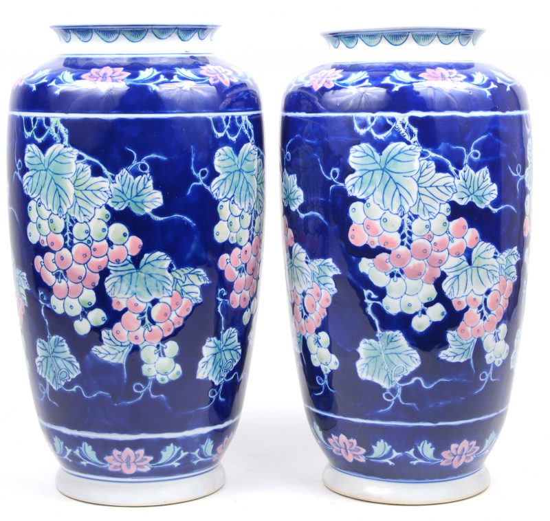 Een paar porseleinen vazen met een meerkleurig decor van druiventrossen op blauwe achtergrond.
