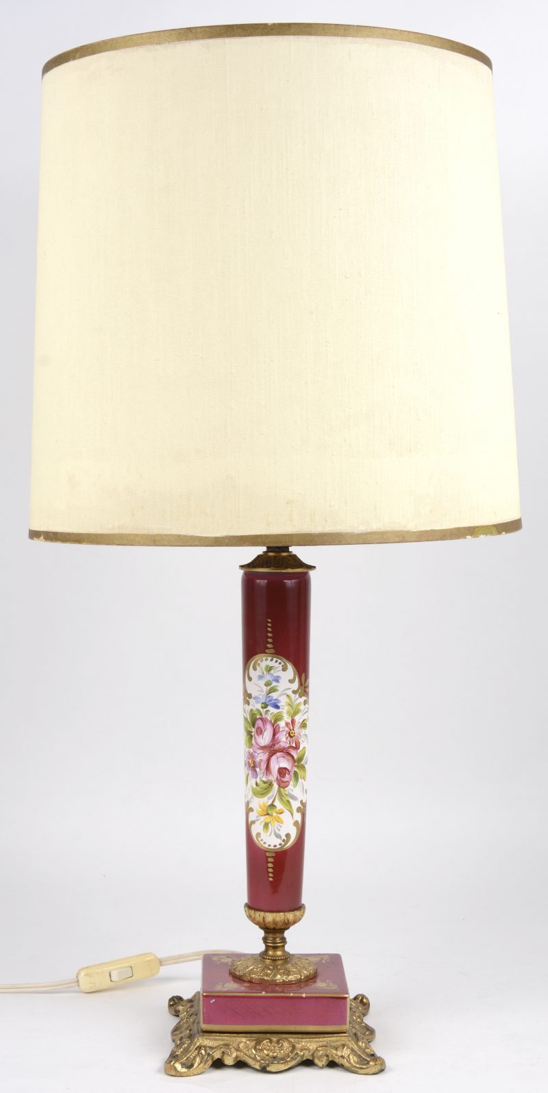 Een porseleinen lampvoet met een meerkleurig bloemendecor in met goud omzoomde cartouche op rode fond en met verguld bronzen voet. Kleine schilfers aan de basis.