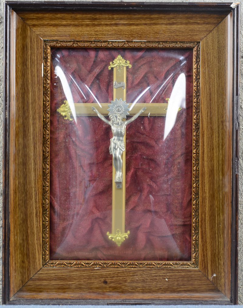 Een messingen kruisbeeld met tinnen Christus. Achter bol glas.