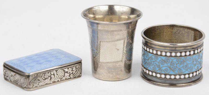 Drie kleine voorwerpen van Russisch zilver, bestaande uit een pillendoosje met email, een servetring, eveneens met email en een vodkabekertje met gegraveerd decor.