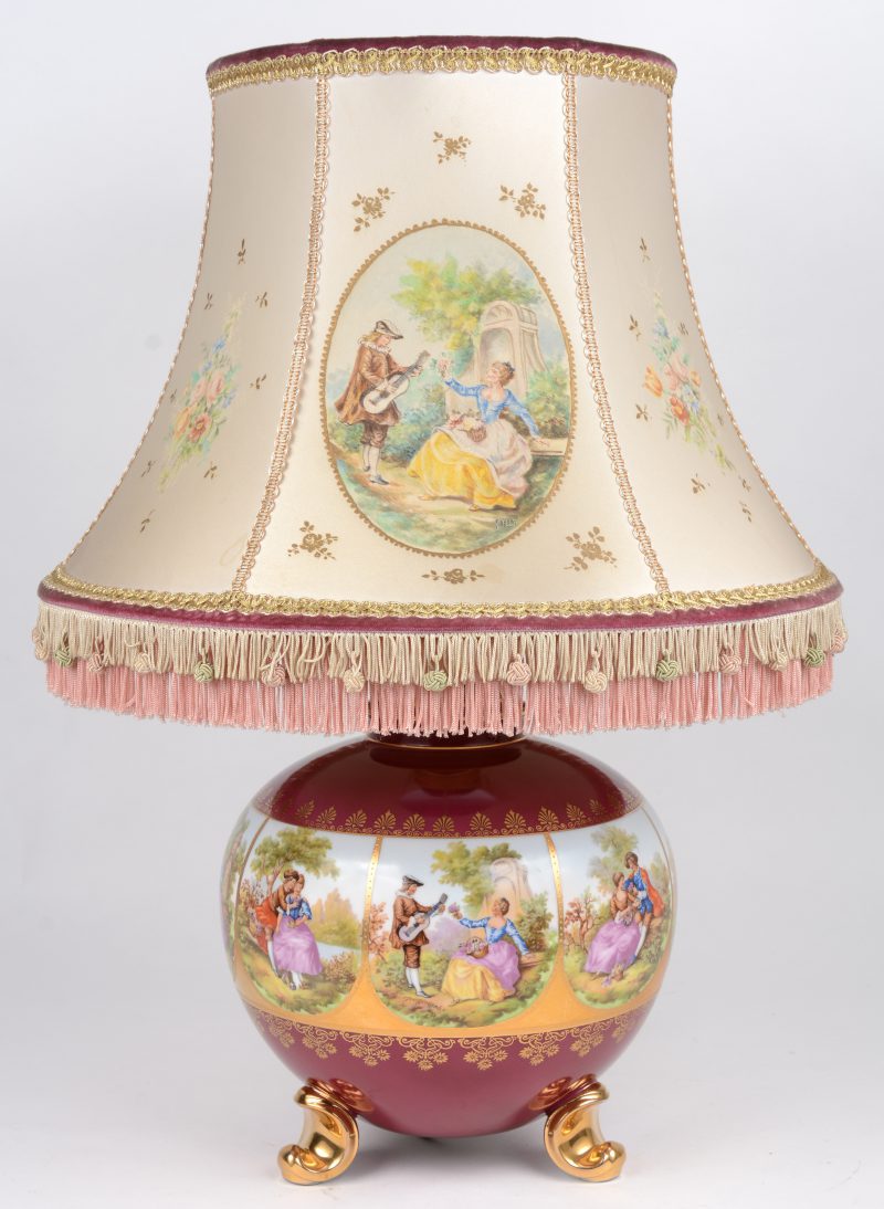 Een bolle lampvoet van Frans porselein met meerkleurige decors naar Fragonard in een Fries, omgeven met vergulde versieringen en op rode fond. Het decor met de hand gereproduceerd op de kap.