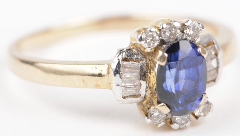 Een 18 K wit en geelgouden ring bezet met briljanten diamant baguetten met een gezamenlijk gewicht van +- 0,40 ct. en een centrale saffier van +- 0,40 ct.