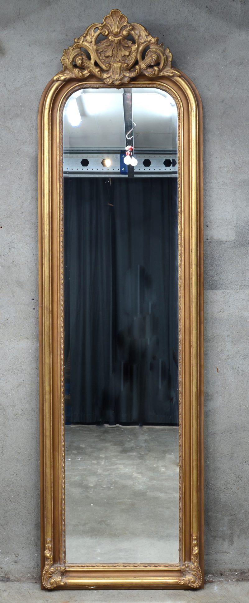 Een hoge spiegel in verguld houten lijst.
