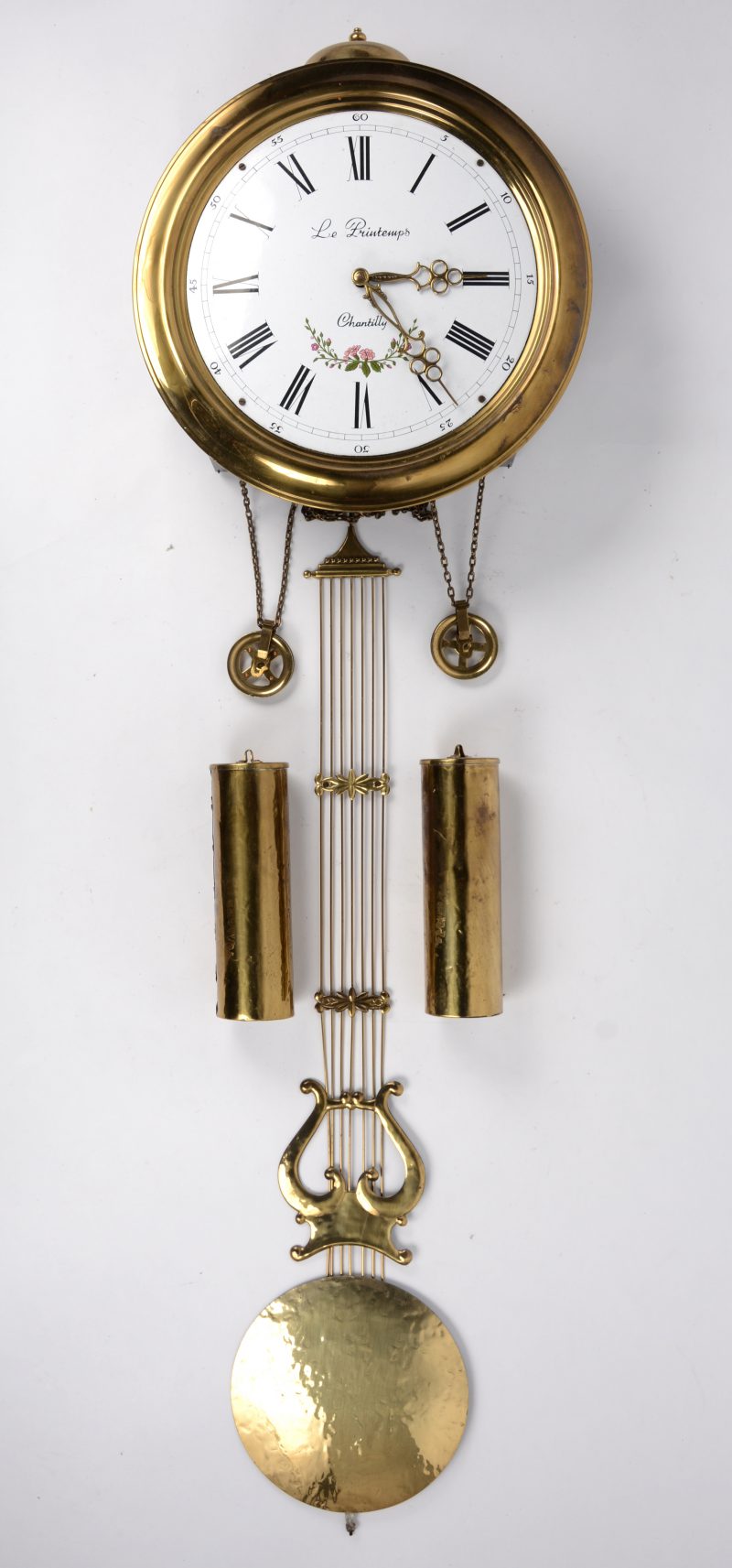 Een Franse stijlklok met een ronde geprofileerde messing rand. De wit emaille wijzerplaat met zwarte Romeinse cijfers. De klok is voorzien van een harpslinger en twee gewichten en met achtdaags uurwerk met belslag.