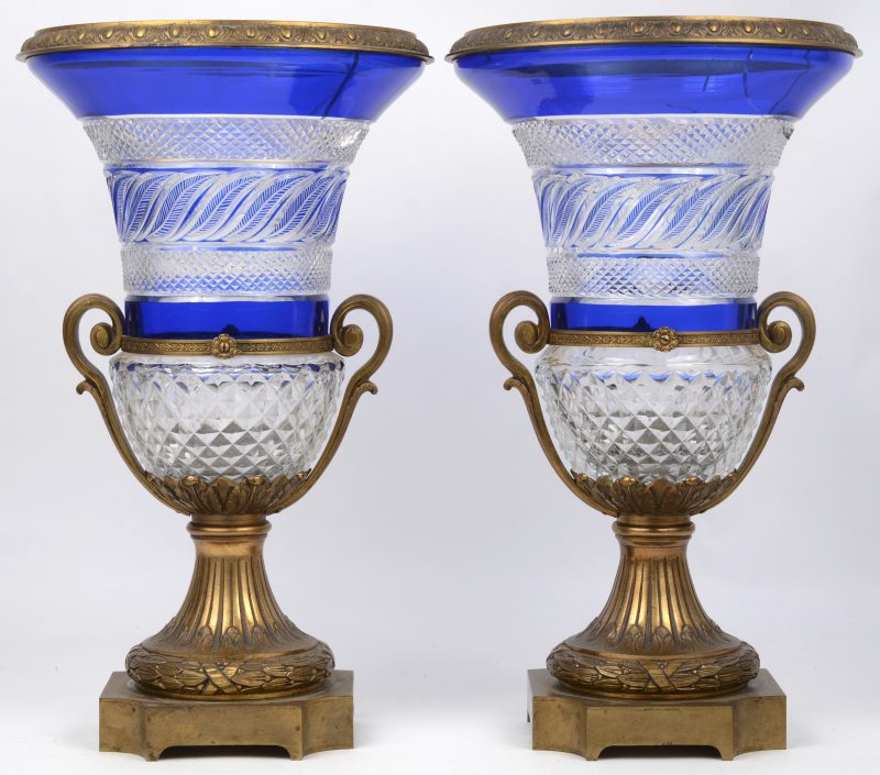 Een paar siervazen van geslepen blauw en kleurloos kristal met bronzen montuur en voet in Lodewijk XVI-stijl. Beide kelken gebarsten.