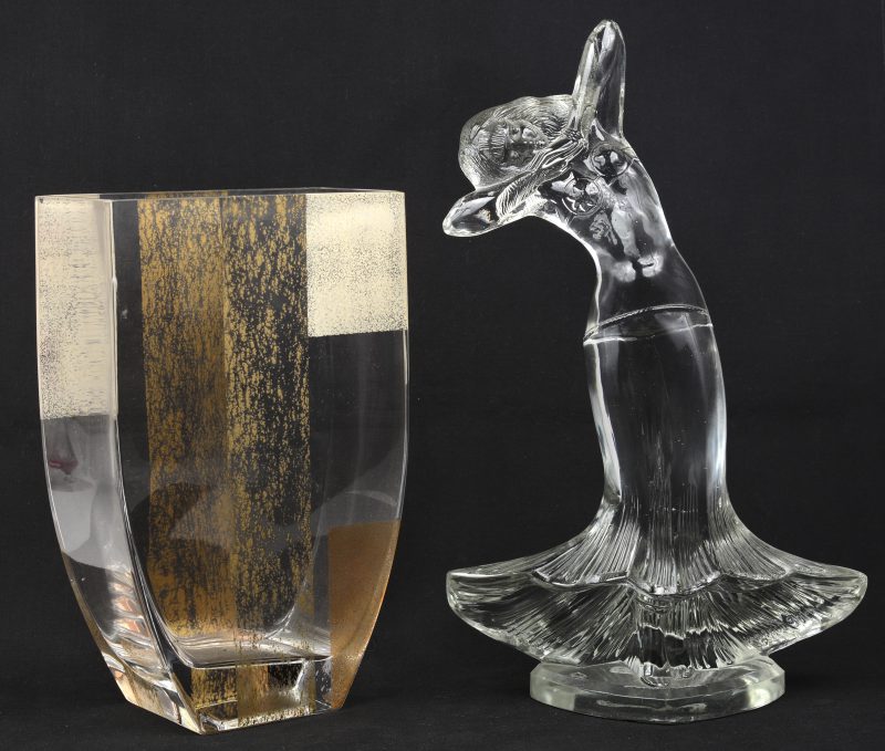 Een platte glazen vaas en een gegoten sierstuk in de vorm van een dansende vrouw.