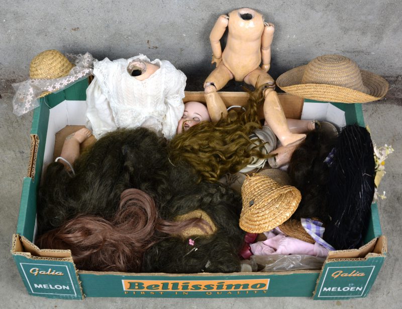 Een doos met poppenpruiken, hoeden, ledematen, een biscuit hoofd e.d.
