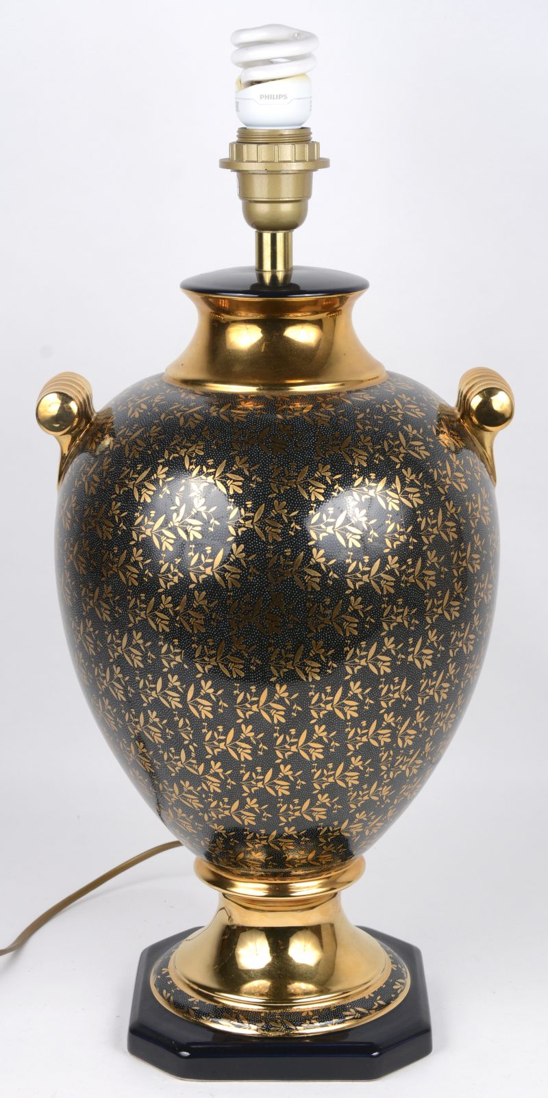 Een porseleinen lampvoet in de vorm van een siervaas, versierd met verguld bladerdecor op donkerblauwe fond. Gesigneerd op de basis.