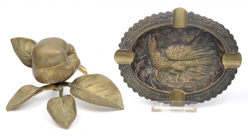Een bronzen asbak met reliëfdecor van een vogel en een dekseldoosje in de vorm van een appel aan een tak.