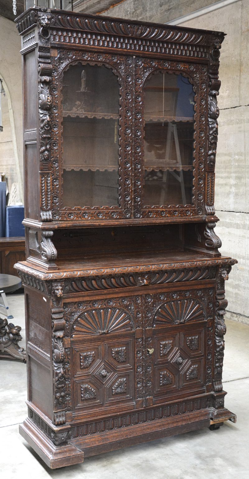 Een tweedelig gebeeldhouwd eikenhouten meubel in Mechelse stijl met onderaan twee paneeldeuren en een lade en bovenaan twee gevitreerde deuren.