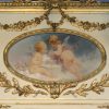 Een spiegel in Louis XVI-stijl met een schilderij met twee engelen in de kuif en versierd met bloemen.