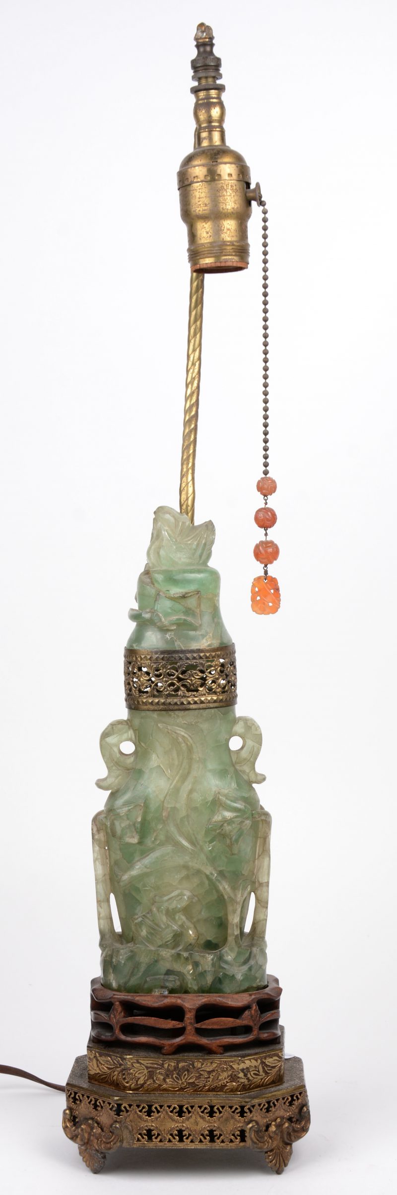 Een gesculpteerd jade sierstuk op voet van messing en hout en gelonteerd als lampje. Deksel gerestaureerd.