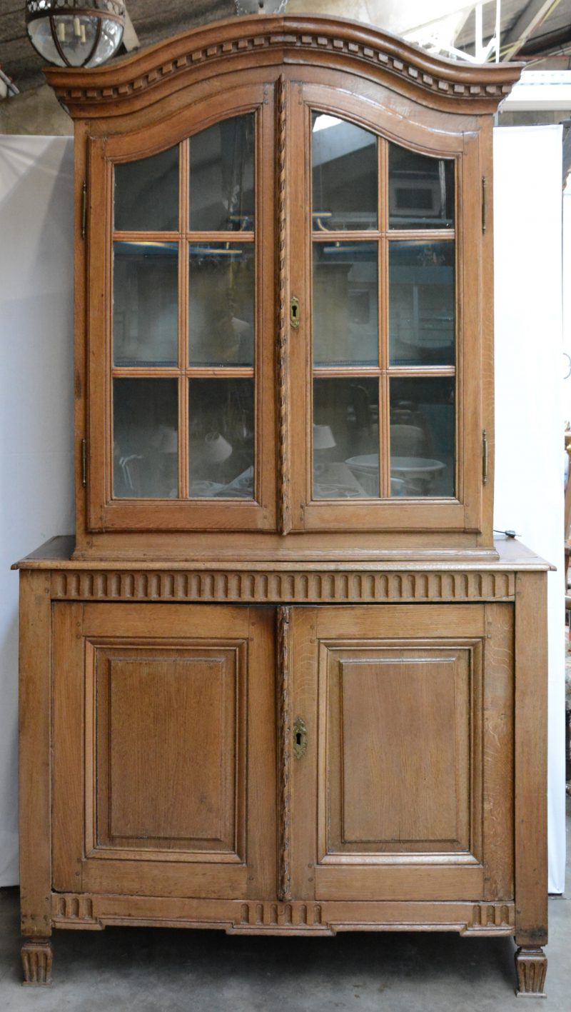 Een tweeledige eikenhouten vitrinekast met twee paneeldeuren onderaan.