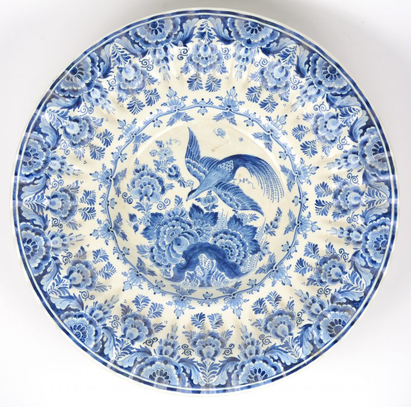 Een grote aardewerken schotel met blauw op wit decor van bloemen en een vogel. Achteraan gemerkt.