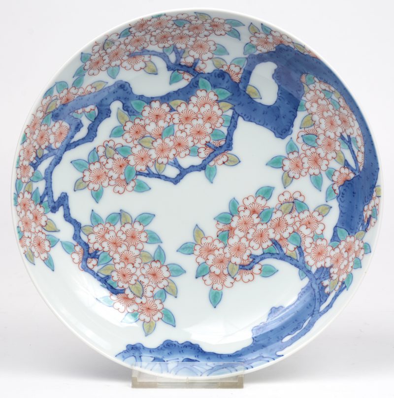 Een bord van Japans porselein met een fijn meerkleurig decor van een bloeiende kerselaar. In fraai etui.