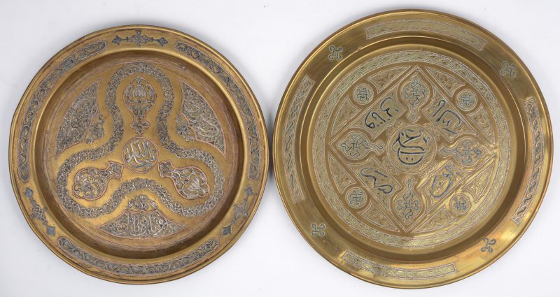 Twee ronde schotels van geel koper, ingelegd met zilver en rood koper en versierd met arabesken en kalligrafie. Midden-Oosten, omstreeks 1900.