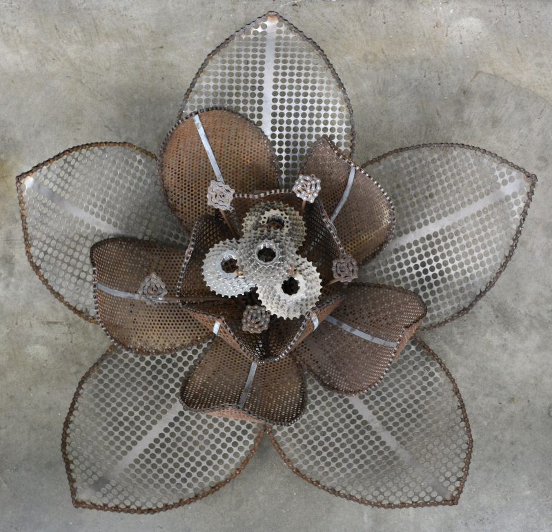 Een bloemvormige wand-/ plafondlamp, opgebouwd uit gerecycleerde materialen zoals tandwielen. Ontwerp van Laurence van Seventer.