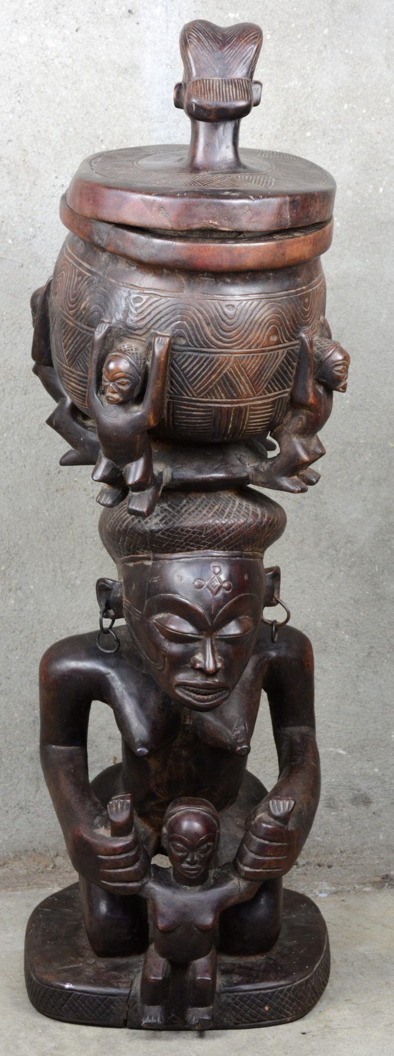 Tchokwe beeld van een moeder met een kind, een voorraadpot op het hoofd. De pot gedragen door vier personages en met een vrouwenhoofd als dekselknop.