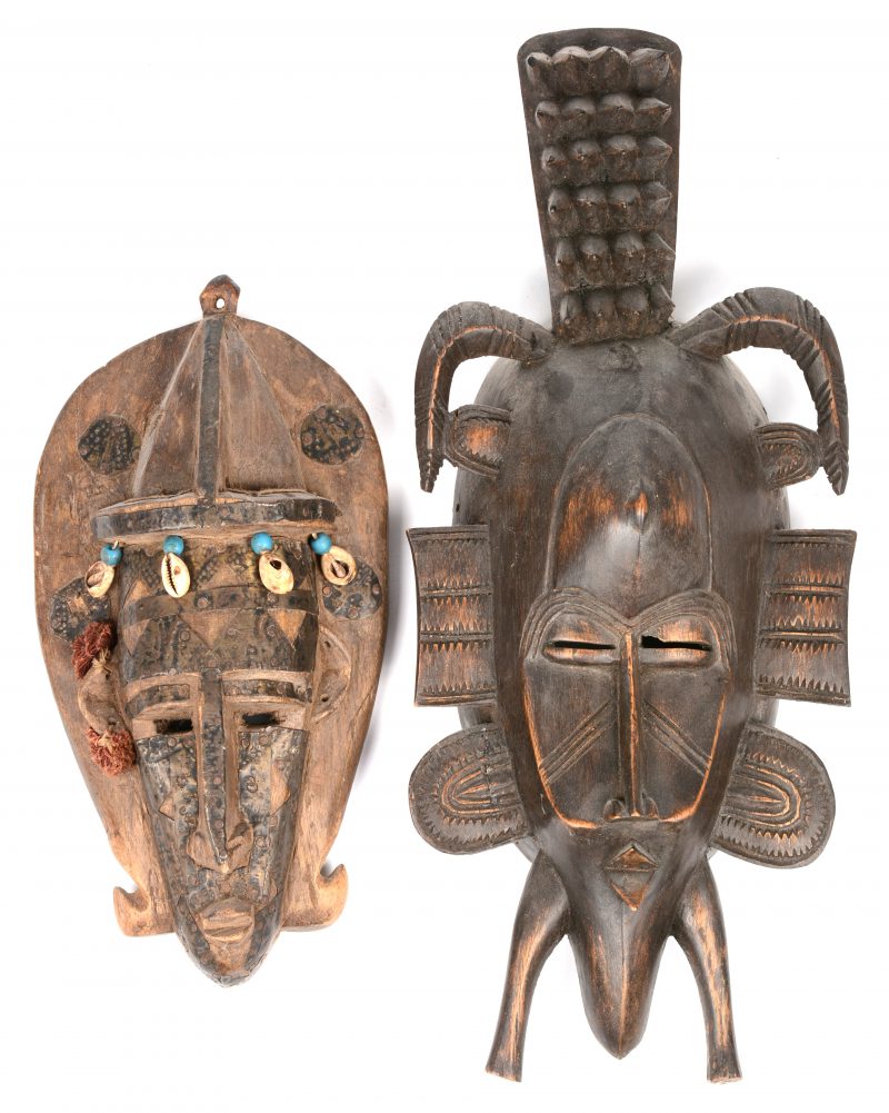 Twee Afrikaans houten maskers, waarbij één met koperen beslag en schelpjes, het andere van de Senoufou in Ivoorkust.