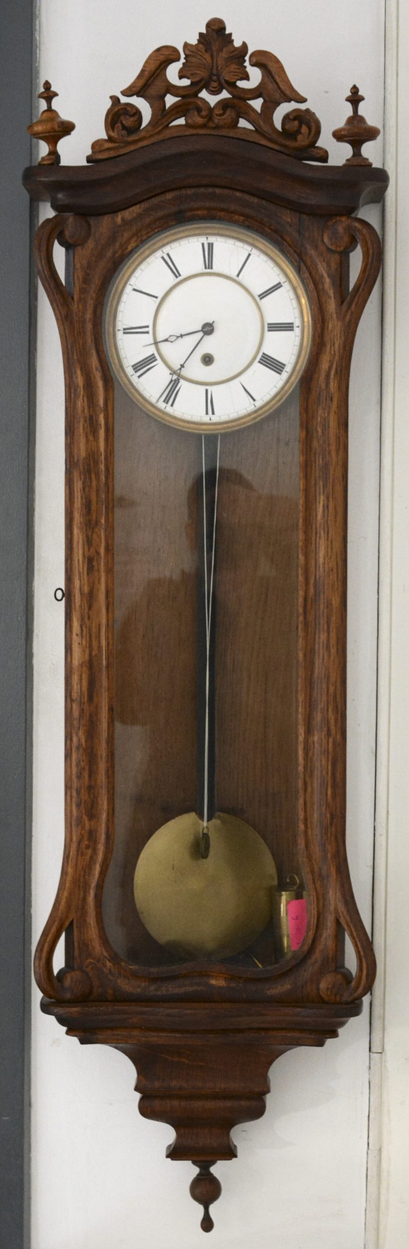Een houten regulateur met gesculpteerde kuif. Met slinger en gewicht.