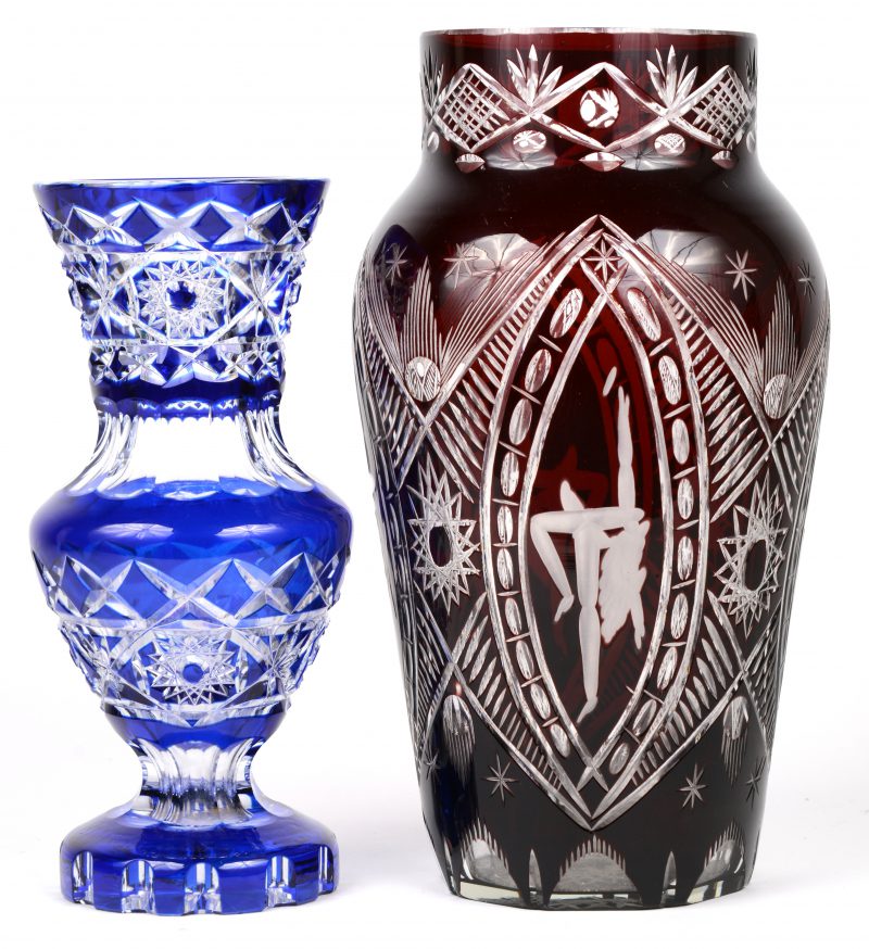 Een kleine vaas op voet van blauw gedubbeld en geslepen kristal. Bijgevoegd een grotere vaas in donkerrood met gelepen decor.