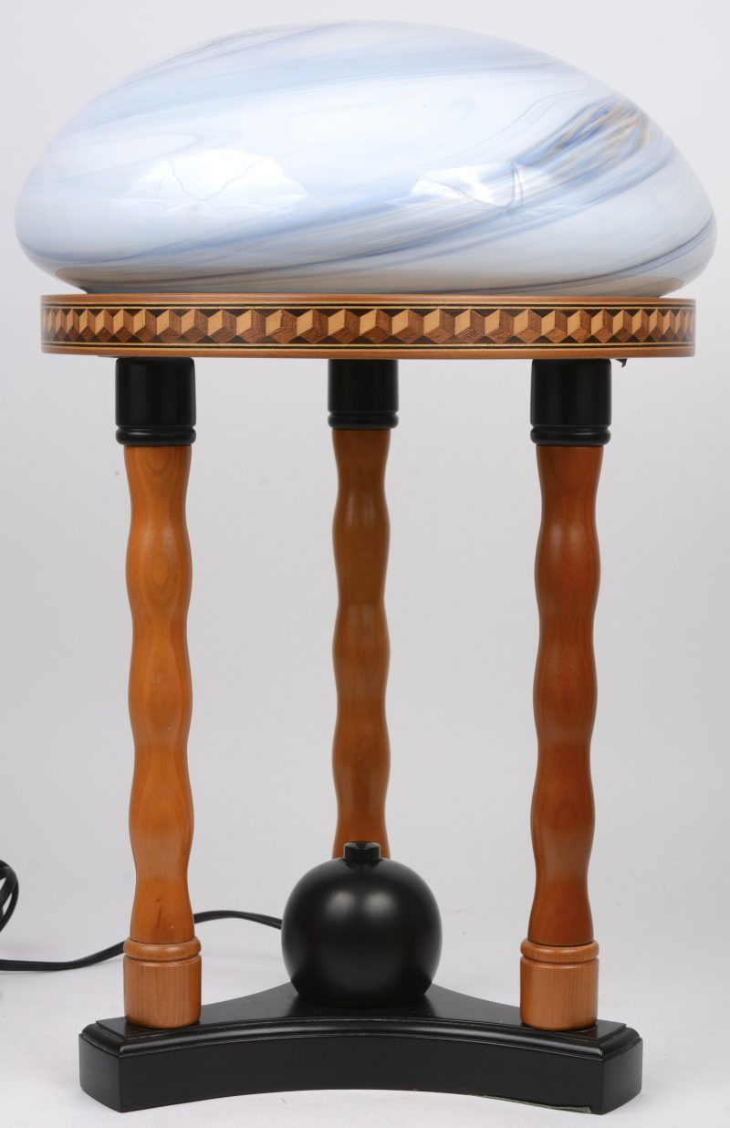 Een recente schemerlamp met gekleurd glazen kap op deels zwartgepatineerd houten voet met drie zuiltjes en de rand versierd met ingelegd kubusmotief.