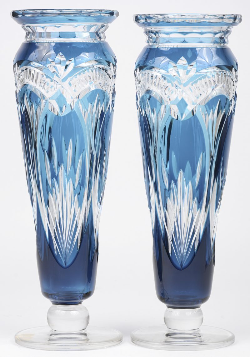 Een paar conische vazen met voetstuk van geslepen kristal, deels in de massa lichtblauw gekleurd. Onderaan gemerkt. En met label.