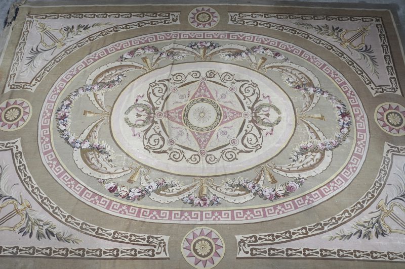 Een XIXe eeuws Europees tapijt met decor van bloemenguirlandes, kwispels en palmtakken. Enkele scheuren en beschadigingen.