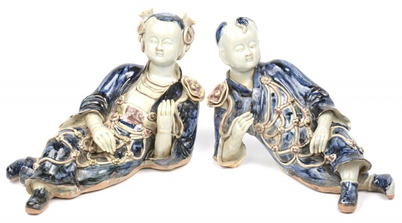 Een paar liggende Chinese figuren van blauw, rood en wit gegeglazuurd porselein.