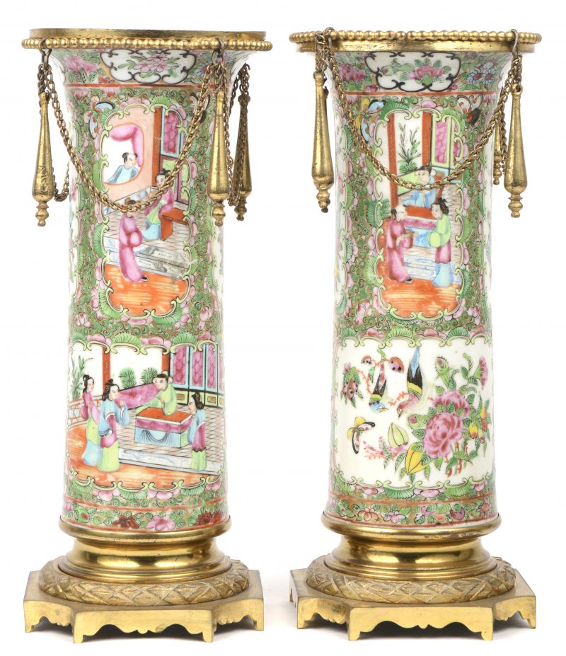 Een paar cilindrische vazen van veelkleurig Chinees porselein met een decor van personages en bloemen in uitsparingen. Canton, XIXde eeuw. Met vergulde bronzen monturen.