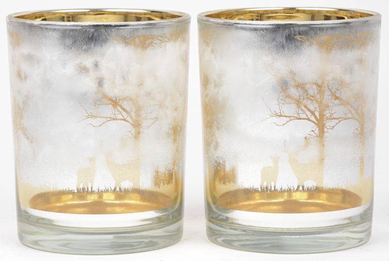 Een paar glazen kaarsenpotjes met gouden decor van bomen en herten.