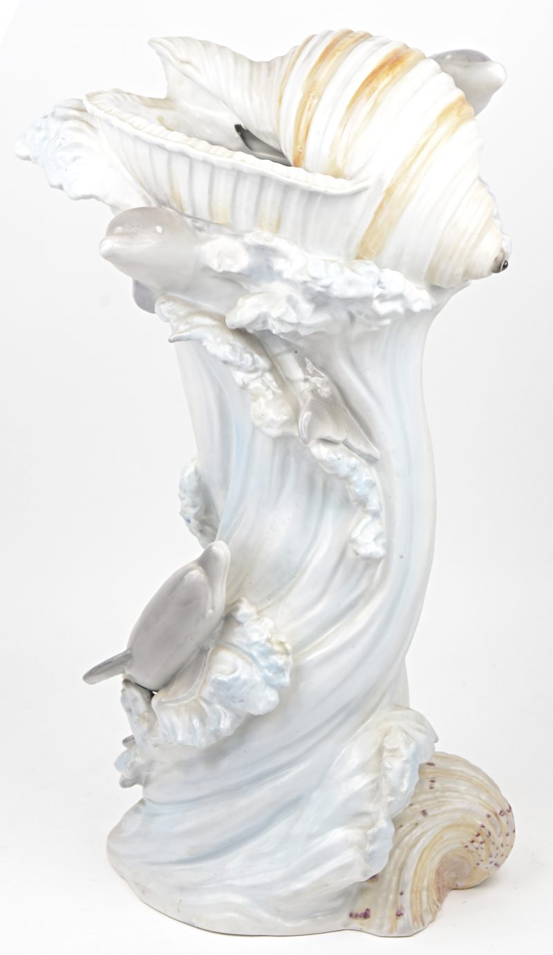 Een meerkleurig porseleinen siervaas in de vorm van een golf met schelpen en dolfijnen.
