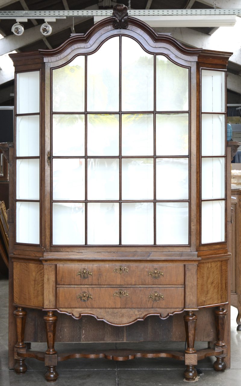 Een tweedelige notenhouten vitrine met onderaan twee brede laden en vier poten met kruisverbinding , bovenaan een brede beglaasde deur met latwerk, schuine zijden. Holland, XIXde eeuw.