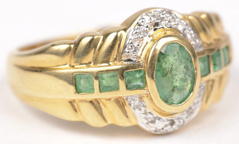 Een 18 K wit en geelgouden ring bezet met kleine briljantjes en een centrale ovale smaragd en baguetten met een gezamenlijk gewicht van +- 0,70 ct.