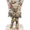 Een siervaas van meerkleurig porselein met bloemendecor en gedragen door twee bronzen engeltjes. Onderaan gemerkt.