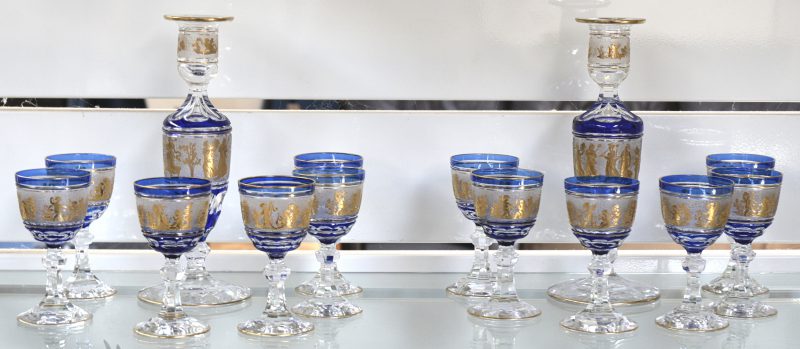 Een reeks van twaalf kleine glaasjes van geslepen kristal. De blauwe kelken versierd met geëtste en vergulde fries van dansende en musicerende putti. Bijgevoegd twee bijpassende kandelaars.