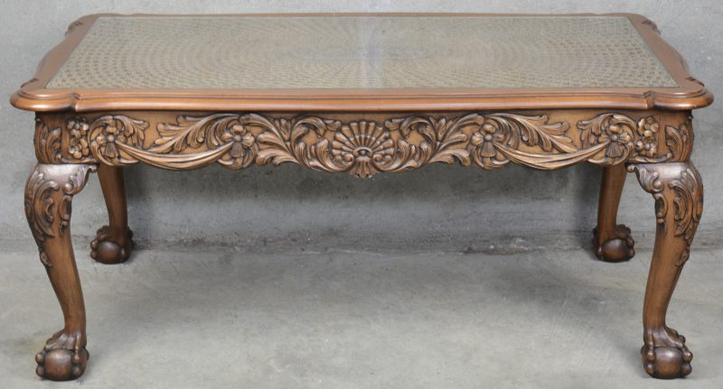 Een gesculpteerde houten salontafel met gecanneerd blad onder glas.