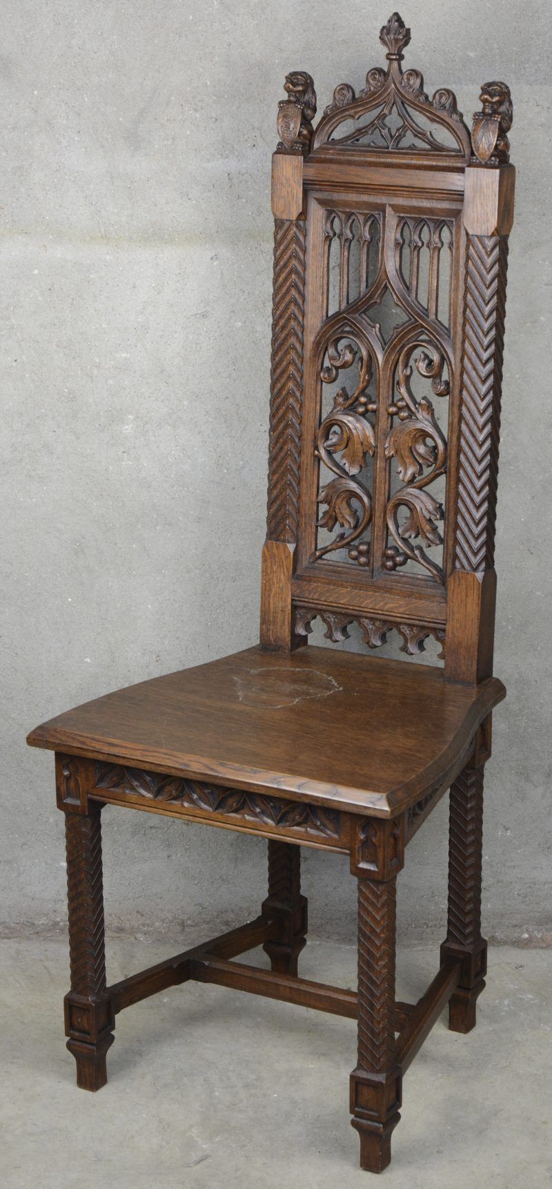 Een eikenhouten stoel in neogotische stijl, versierd met gesculpteerde leeuwtjes met schild op de rug.