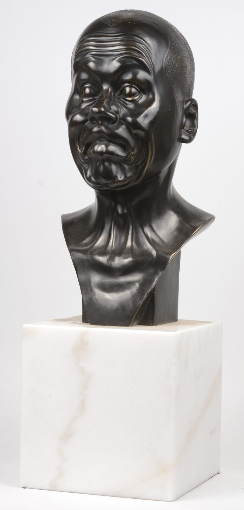 “Charakterkopf””. Een expressieve bronzen buste op een wit marmeren sokkel. Naar het voorbeeld van Franz Wavier Messerschmitt.